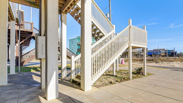 Un espace extérieur abrité, doté d’un escalier et de rampes en bois, d’un sol en béton et surplombé d’un ciel dégagé.