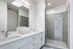 Une salle de bain moderne avec deux lavabos, un grand miroir et une douche à parois de verre.