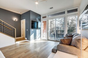 Un vaste espace de vie doté d’un plancher en bois, d’un mur gris et d’une grande porte-fenêtre coulissante donnant sur une terrasse extérieure.