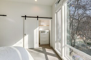 Une chambre avec une grande fenêtre, un lit, une armoire et une porte donnant sur une salle de bain.