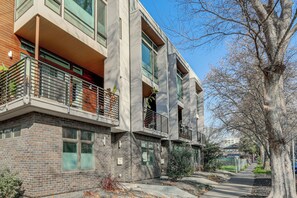 Un immeuble moderne à plusieurs étages, doté de balcons, d’une façade en briques et situé dans une rue bordée d’arbres.