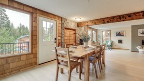 A spacious dining area with a large wooden table and chairs, a stone accent wall, and large windows offering a view of the outdoors.