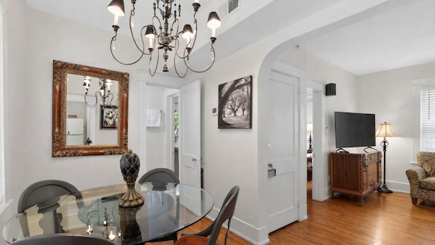 A dining area with a glass table, chairs, a chandelier, a mirror, and a painting. - Pet Friendly Midtown Mobile Condo (Mobile)