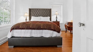 A bedroom with a large bed, two bedside tables with lamps, a window with blinds, and a door. - Pet Friendly Midtown Mobile Condo (Mobile)