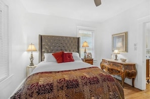 A bedroom with a large bed, two bedside tables with lamps, a wooden dresser, and a mirror on the wall. - Pet Friendly Midtown Mobile Condo (Mobile)