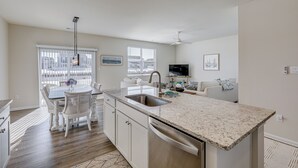 A modern kitchen with a central island, white cabinetry, and a dining area with a table and chairs. - Shuttle to the Beach! Spacious Home in Millville (Millville)