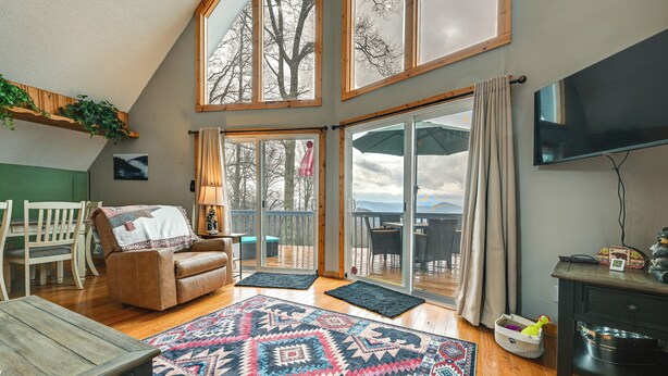 A spacious living room with a large window, a brown leather sofa, a wooden coffee table, and a patterned rug.