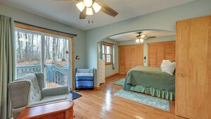 A bedroom with a wooden floor, a bed with green bedding, a wooden wardrobe, a chair, and a window with a view of trees.