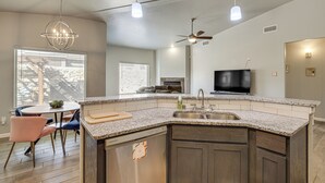 Une cuisine moderne dotée de plans de travail en granit, d’un lave-vaisselle encastré, d’un grand îlot central et d’un ventilateur de plafond.