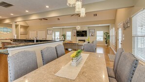 Una cocina amplia con una isla central, un comedor con mesa de mármol y una sala de estar con televisor y obras de arte.