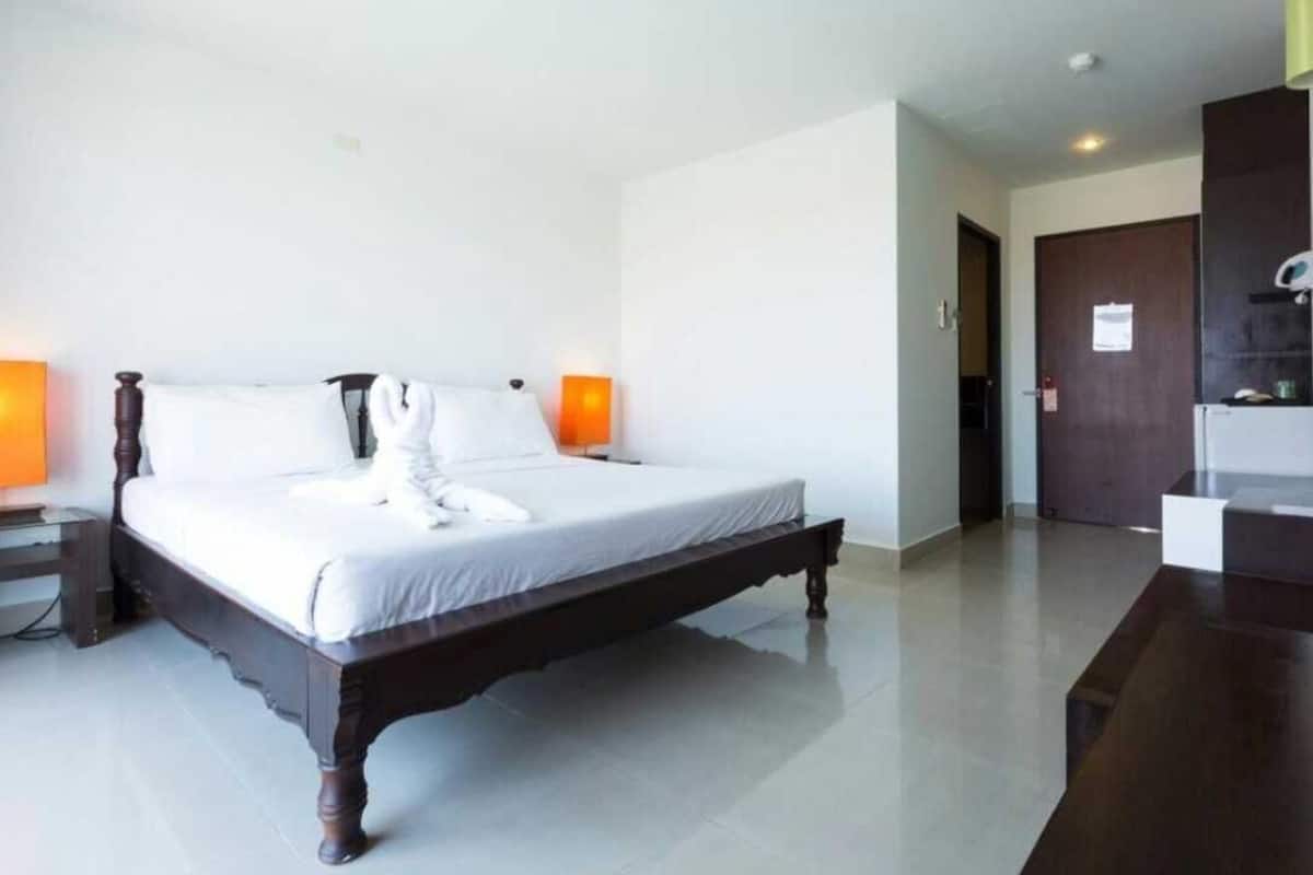 A neatly made bed with white linens and a towel, a wooden nightstand with a lamp, and a dark wooden dresser.