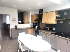 A modern kitchen with a white dining table, grey cabinets, and a black backsplash.