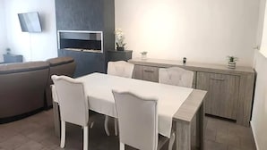 A modern kitchen with a dining area, featuring a built-in oven, white chairs, and a grey cabinet. - Welcome to our Mouscron Cocoon (Mouscron)