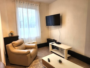 A living room with a leather sofa, a TV mounted on the wall, a small table with a remote control, and a decorative bowl on the table.