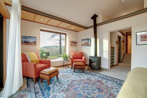 A living room with a large window, a fireplace, and a staircase leading to another level. - On 10 Acres! Serene Nevada City Retreat w/ Hot Tub (Nevada City)