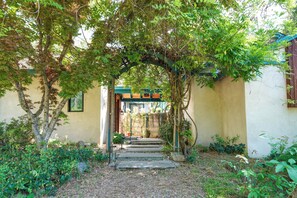 A stone pathway leading to a wooden door under a green archway, surrounded by greenery and a building with a blue roof. - On 10 Acres! Serene Nevada City Retreat w/ Hot Tub (Nevada City)
