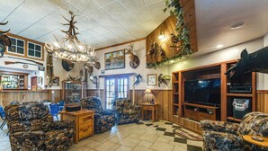 Un salon spacieux, agrémenté de meubles à motifs, d’un lustre, de têtes d’animaux empaillées et d’un téléviseur.