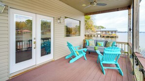 A covered deck with a view of a dock and water, featuring turquoise Adirondack chairs and a sofa with patterned cushions. - Wake Up on the Water! Lake Tyler East Hideaway (Troup)