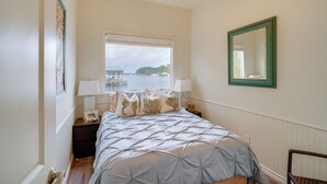 A bedroom with a bed, two bedside tables with lamps, a window with a view of a dock and water, and a mirror on the wall. - Wake Up on the Water! Lake Tyler East Hideaway (Troup)