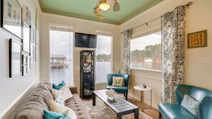 A living room with a sofa, armchairs, a coffee table, and a TV. There is a view of a lake and a dock outside. - Wake Up on the Water! Lake Tyler East Hideaway (Troup)