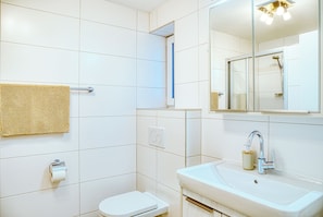 Ein modernes Badezimmer mit weißen Fliesen, Toilette, Waschbecken mit Spiegel und Dusche.