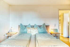 Ein Doppelbett mit Holz-Kopfteil, zwei Nachttische, eine Nachttischlampe und ein kleines, an der Wand befestigtes Regal mit einem Schild.