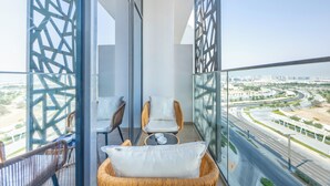 Un balcon avec des fauteuils en osier, une petite table et une vue sur le paysage urbain, avec une route et de la verdure.