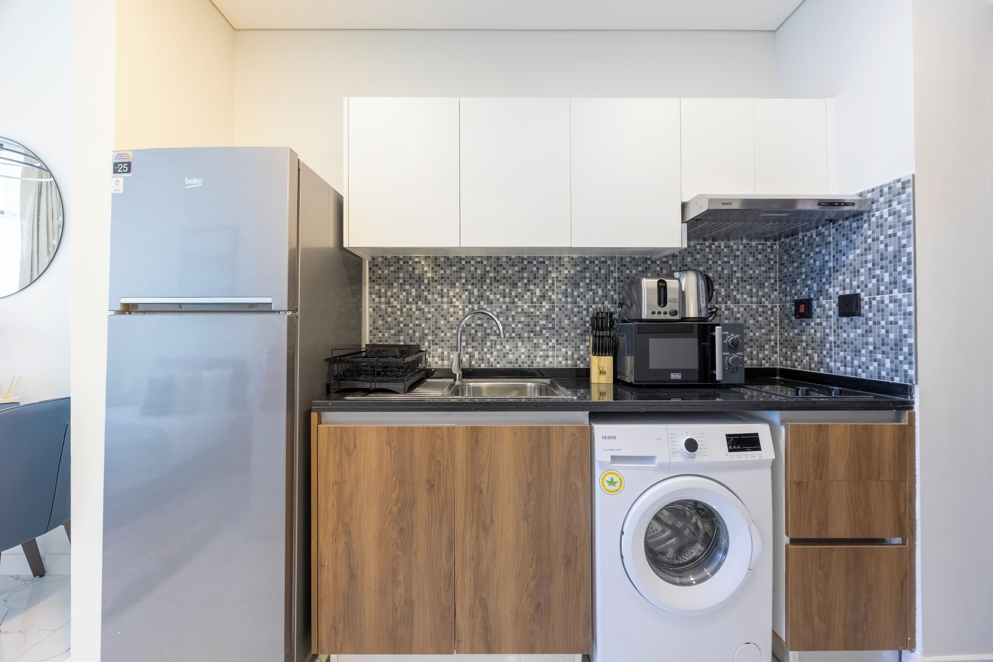 Een compacte keuken met een koelkast, magnetron, broodrooster, spoelbak en wasmachine.