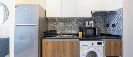 Een compacte keuken met een koelkast, magnetron, broodrooster, spoelbak en wasmachine.
