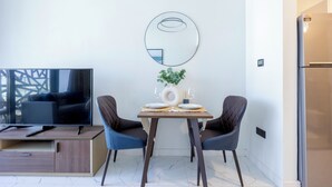 Un salon moderne doté d’un téléviseur à écran plat, d’une table à manger avec deux chaises, d’un miroir et d’un réfrigérateur.