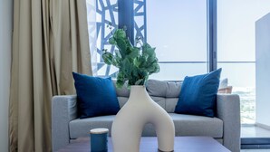 Un salon moderne avec un canapé gris, des coussins bleus, un vase blanc contenant des plantes vertes et une table basse en bois.