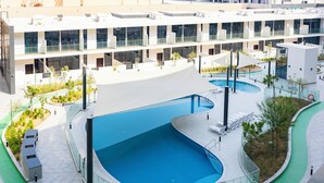 Un bâtiment moderne doté d’une grande piscine à bords incurvés, entourée d’une promenade verdoyante.