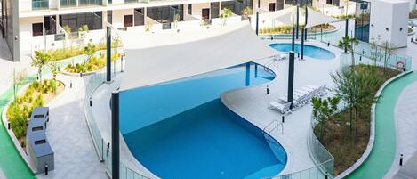 Un edificio moderno con una gran piscina curvada rodeada por un camino verde.