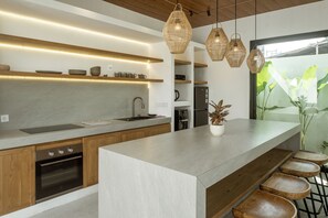Eine moderne Küche mit einer großen Kochinsel, Holzschränken und Pendelleuchten.