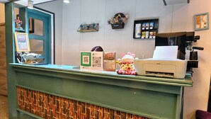 Ein Empfangsschalter mit grüner Theke, eine Wand mit Ziegeloptik, ein Schild mit einem QR-Code, eine Kaffeemaschine und eine Speisekarte.