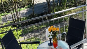 A balcony with two chairs, a table, and a vase with flowers. - Large 120sqm apartment -balcony side view to the stream-2 Bāder- nature & hiking (Witzenhausen)