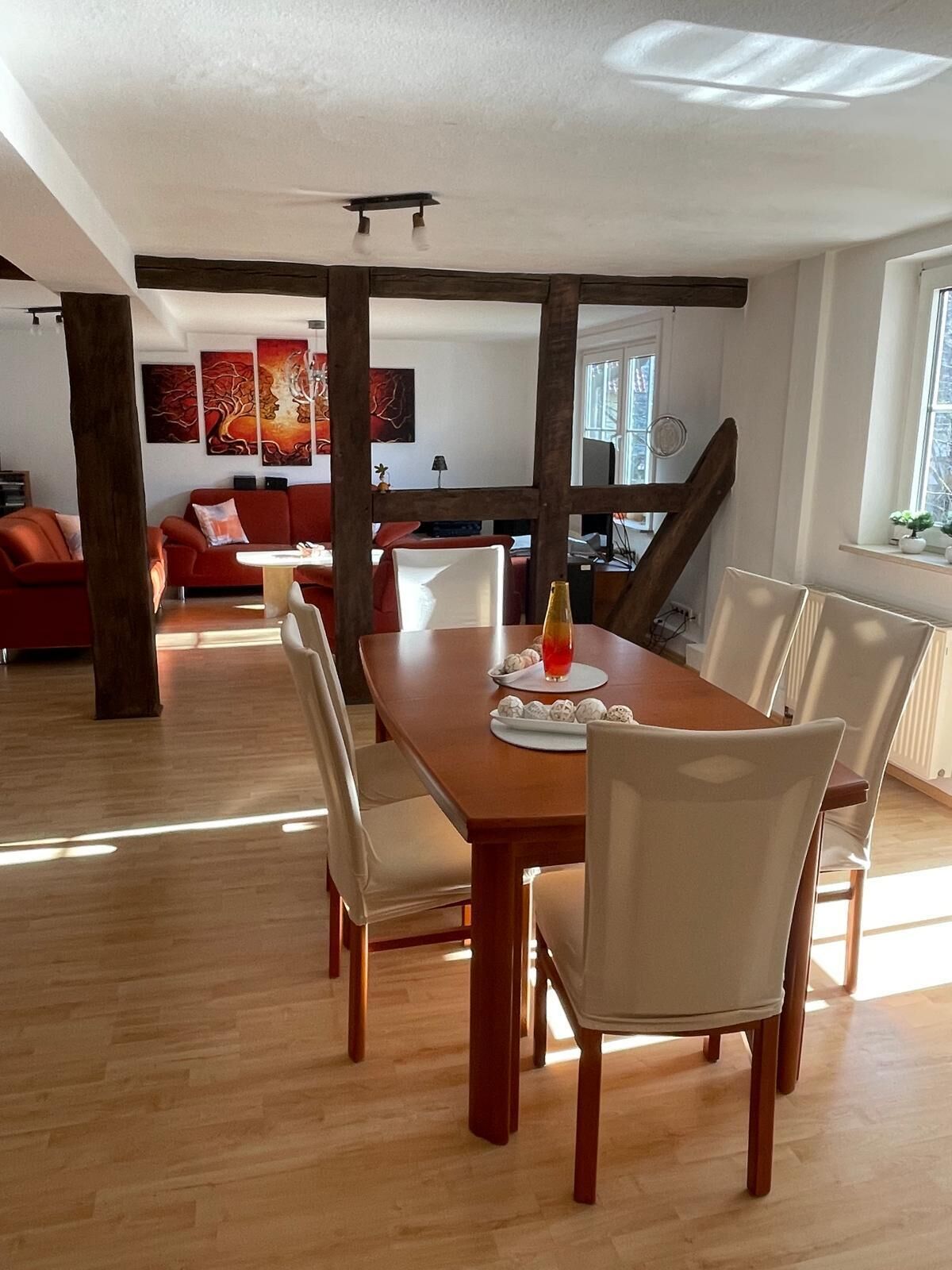 A dining area with a wooden table, white chairs, and a red sofa. - Large 120sqm apartment -balcony side view to the stream-2 Bāder- nature & hiking (Witzenhausen)