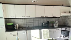 A modern kitchen with white cabinets, a black countertop, and a dining table with chairs. - Large 120sqm apartment -balcony side view to the stream-2 Bāder- nature & hiking (Witzenhausen)