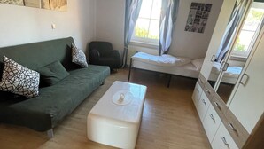 A room with a green sofa, a white ottoman, a bed, a chair, and a wardrobe. - Large 120sqm apartment -balcony side view to the stream-2 Bāder- nature & hiking (Witzenhausen)