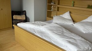 A single bed with a wooden frame and white bedding in a room with light wooden flooring and a wooden wardrobe with shelves. - Large 120sqm apartment -balcony side view to the stream-2 Bāder- nature & hiking (Witzenhausen)
