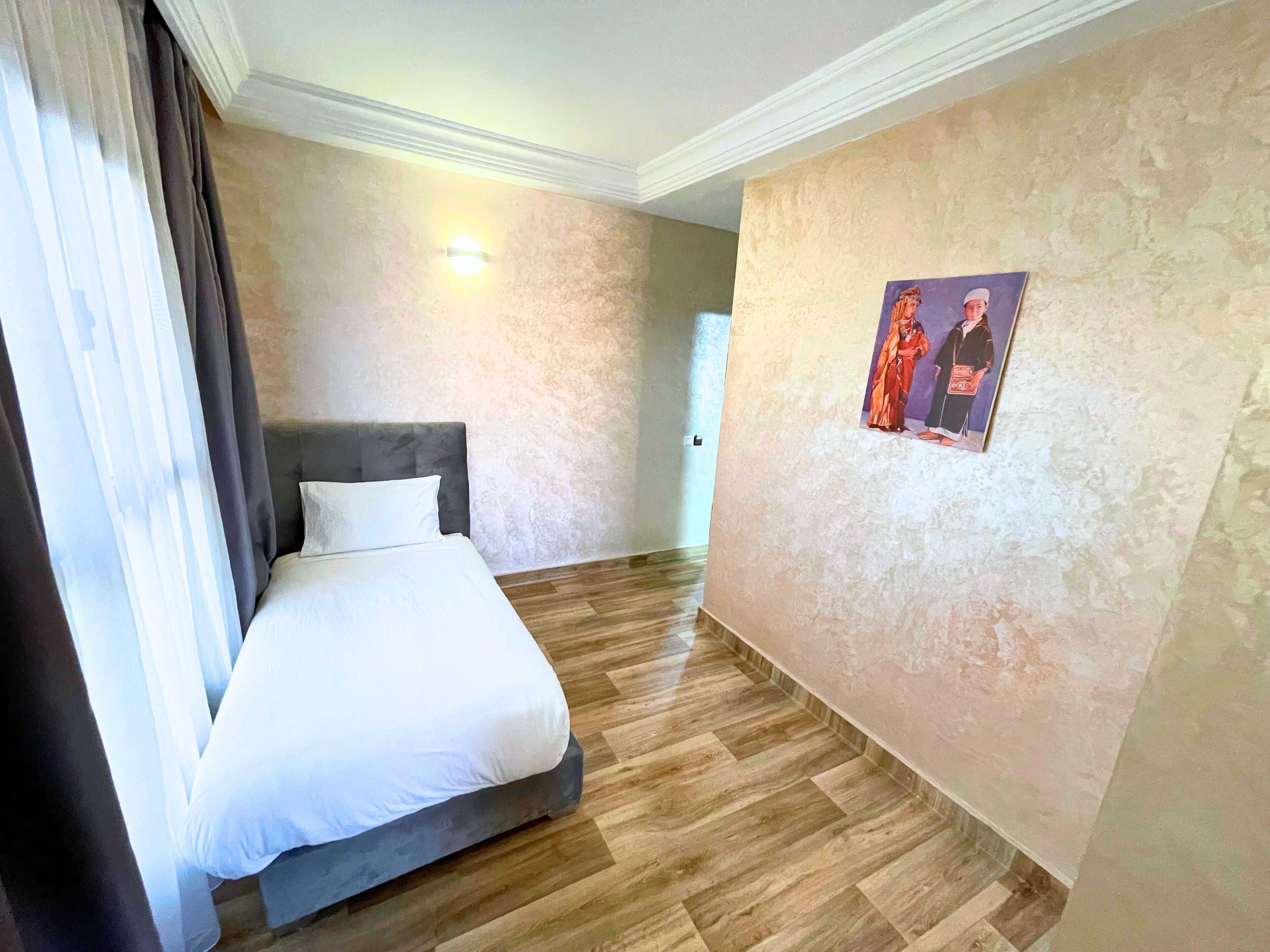 Een hotelkamer met een bed, houten vloeren, een lichtgekleurde wand en een schilderij.