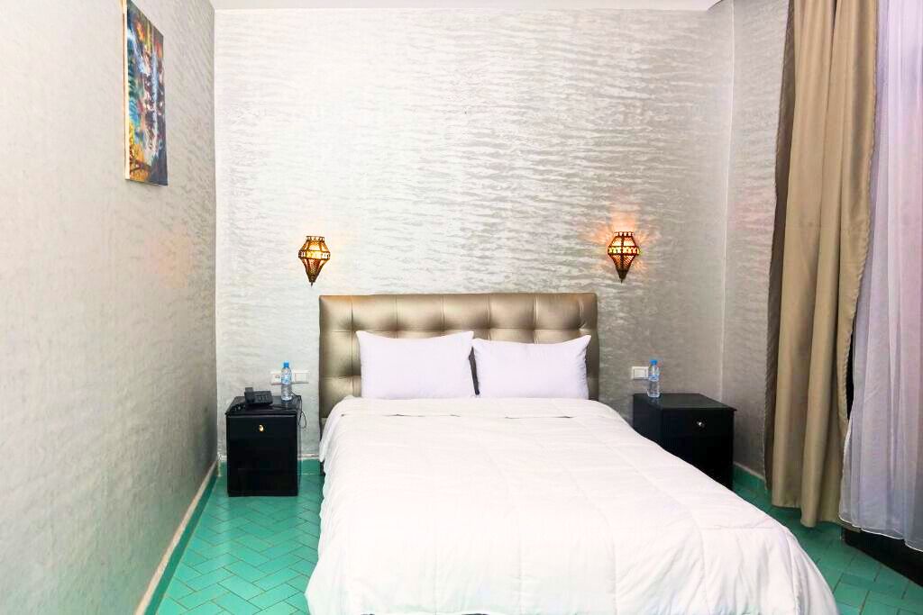 A hotel room with a tufted headboard, two bedside tables with lamps, a bed with white bedding, and a green tiled floor.