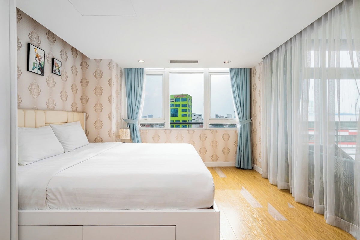 A bedroom with a bed, a window with curtains, and a view of a building outside.
