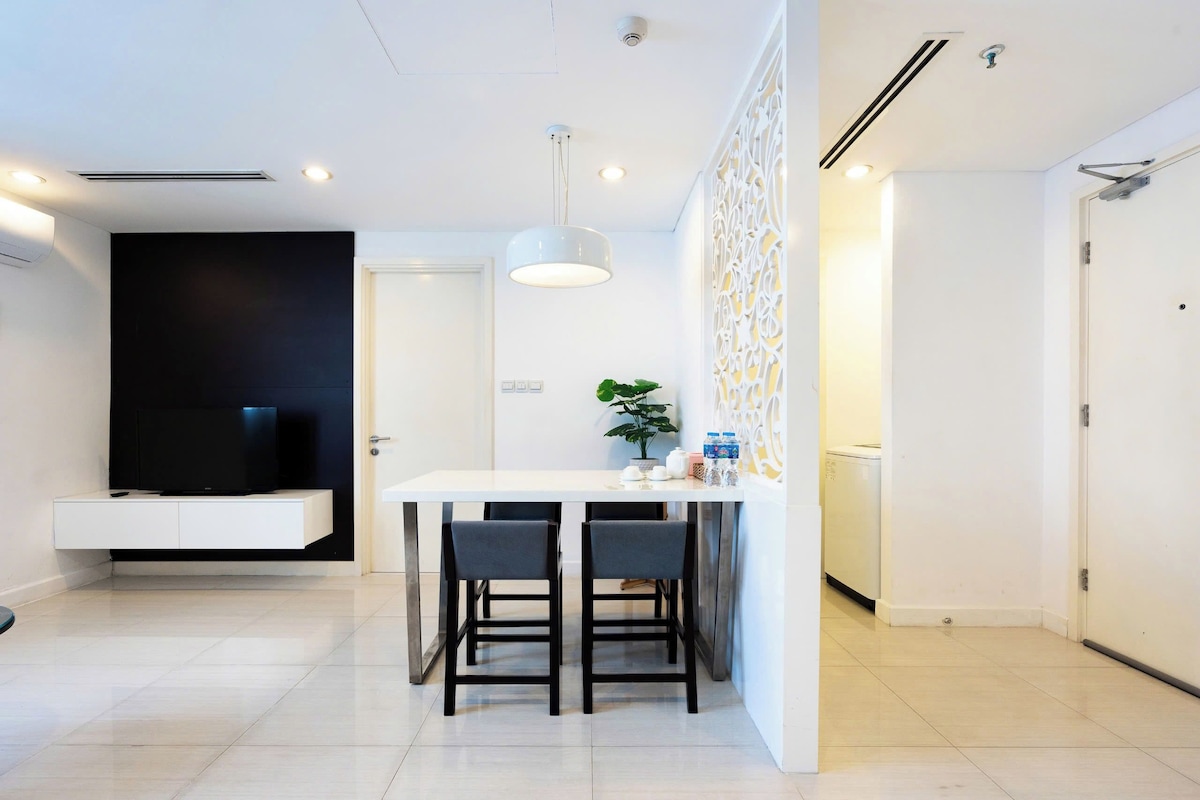 A modern kitchen with a white countertop, two black chairs, a hanging pendant light, and a built-in oven.