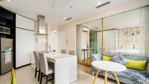Eine moderne Küche mit weißen Schränken, einer eingebauten Mikrowelle und einem Kühlschrank. Es gibt einen Essbereich mit einem weißen Tisch und Stühlen, sowie eine Couch mit gemusterten Kissen.
