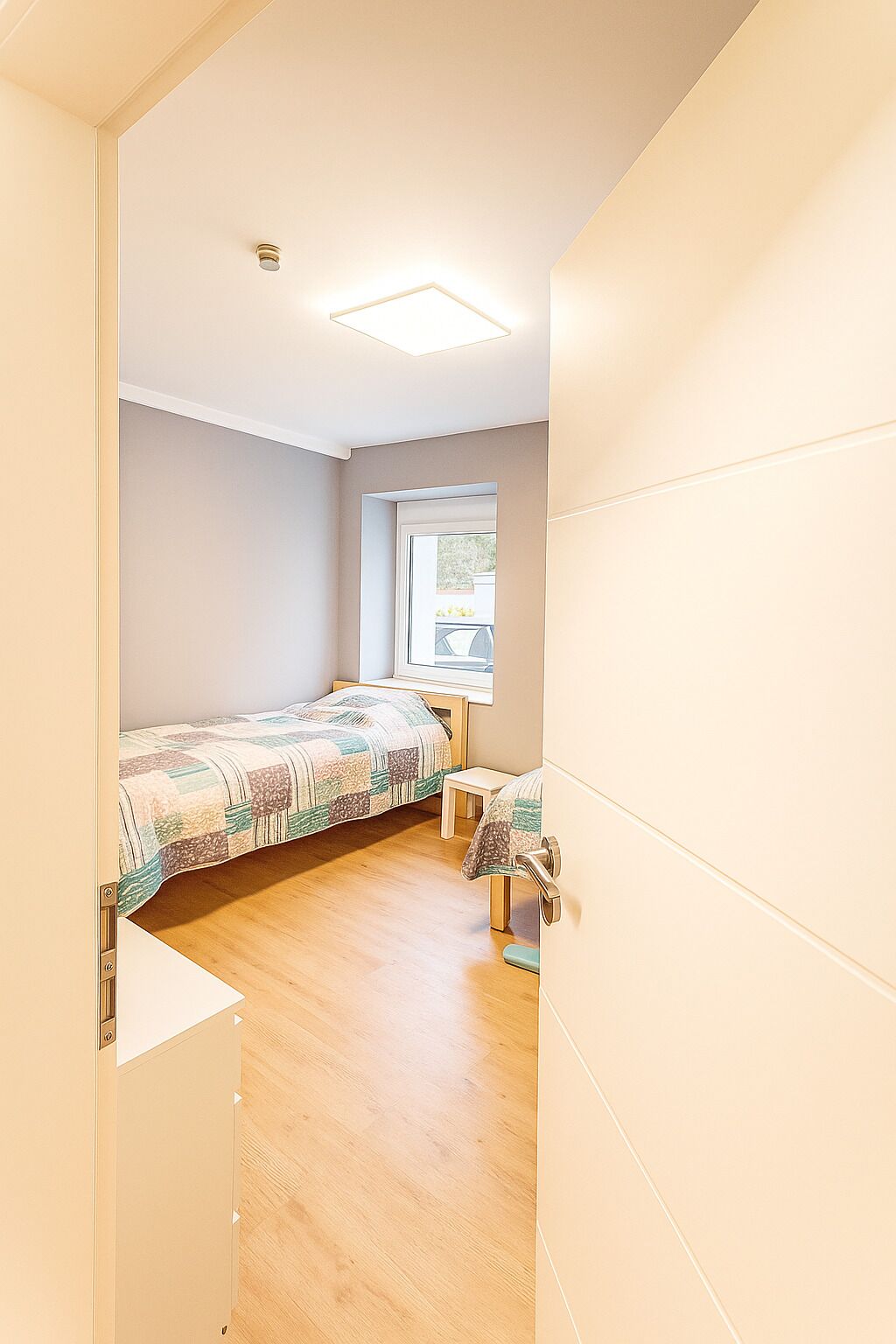 A compact bedroom with a single bed, a small table, and a window.