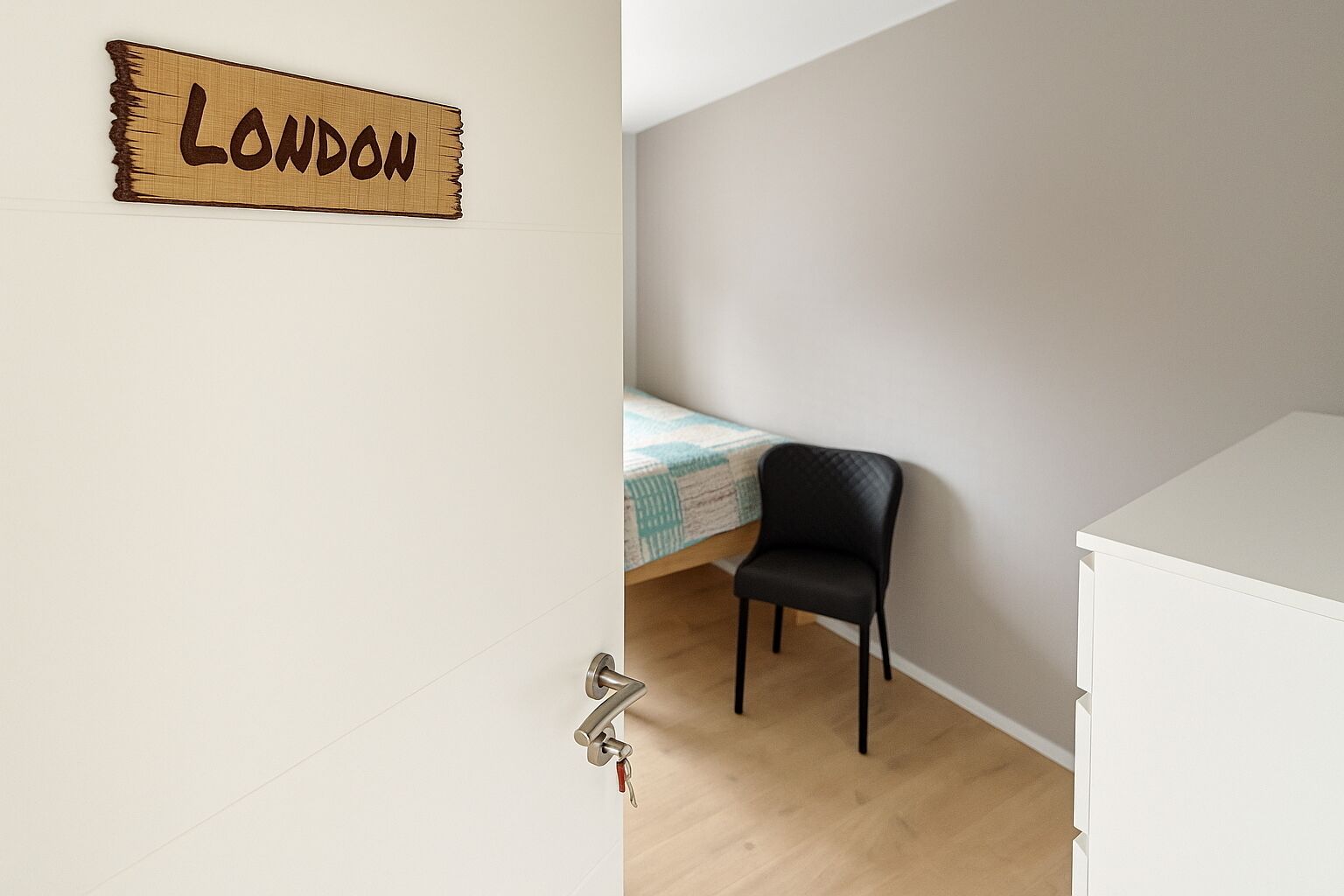 A room with a bed, a chair, a white dresser, and a wall sign that reads "LONDON".