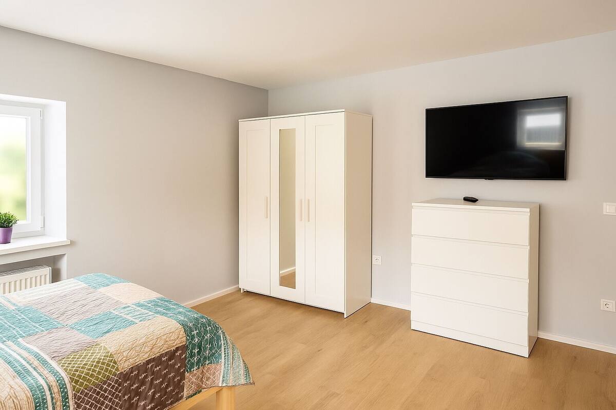 Une chambre avec un lit, une armoire, une télévision et une fenêtre agrémentée d’une plante.