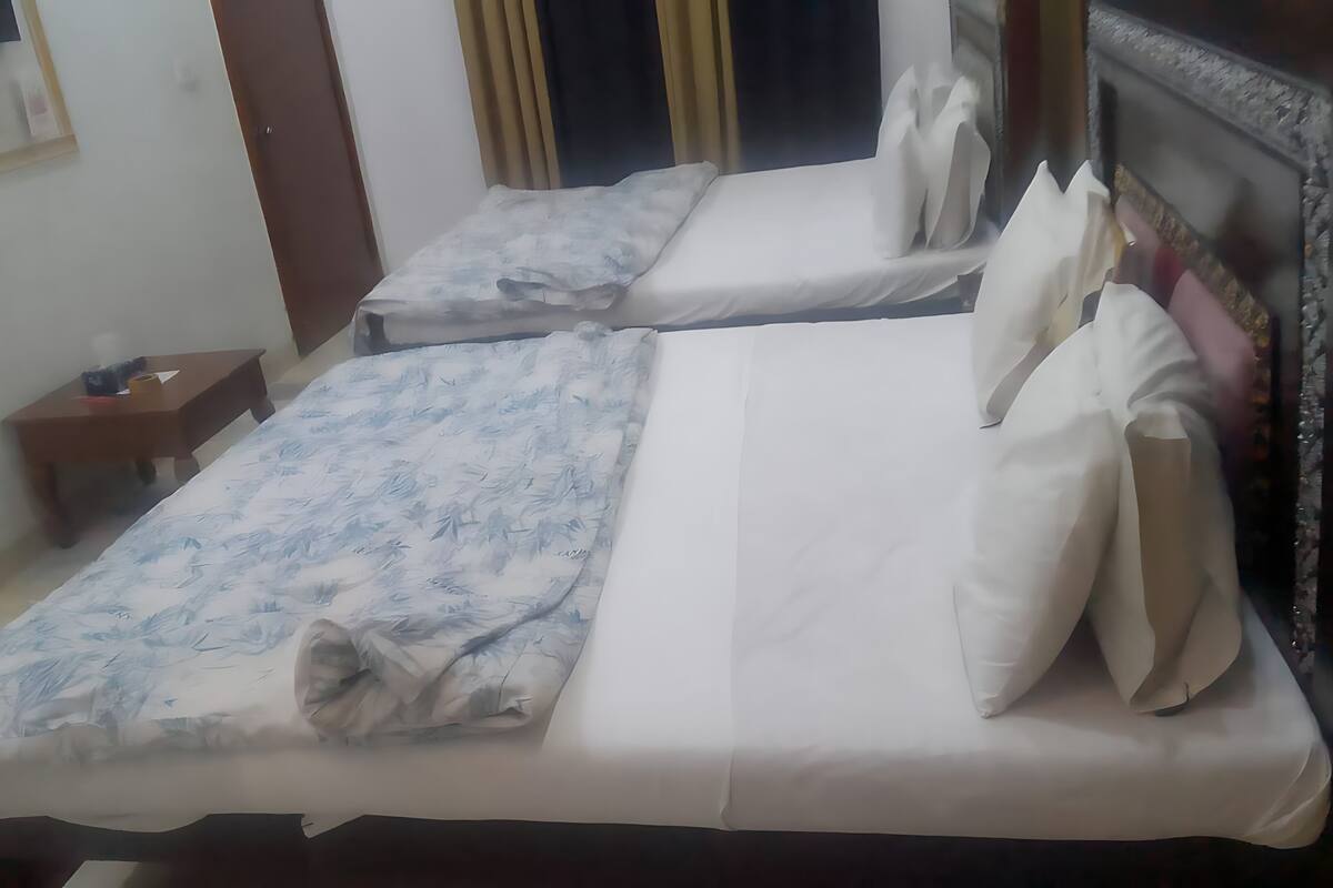 A hotel room with two beds, a wooden nightstand, a wall-mounted TV, and a window with curtains.