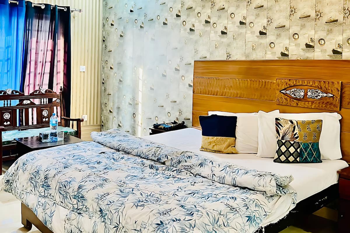A hotel room with a large bed, a wooden headboard, a ceiling fan, and a wall with nautical-themed wallpaper.